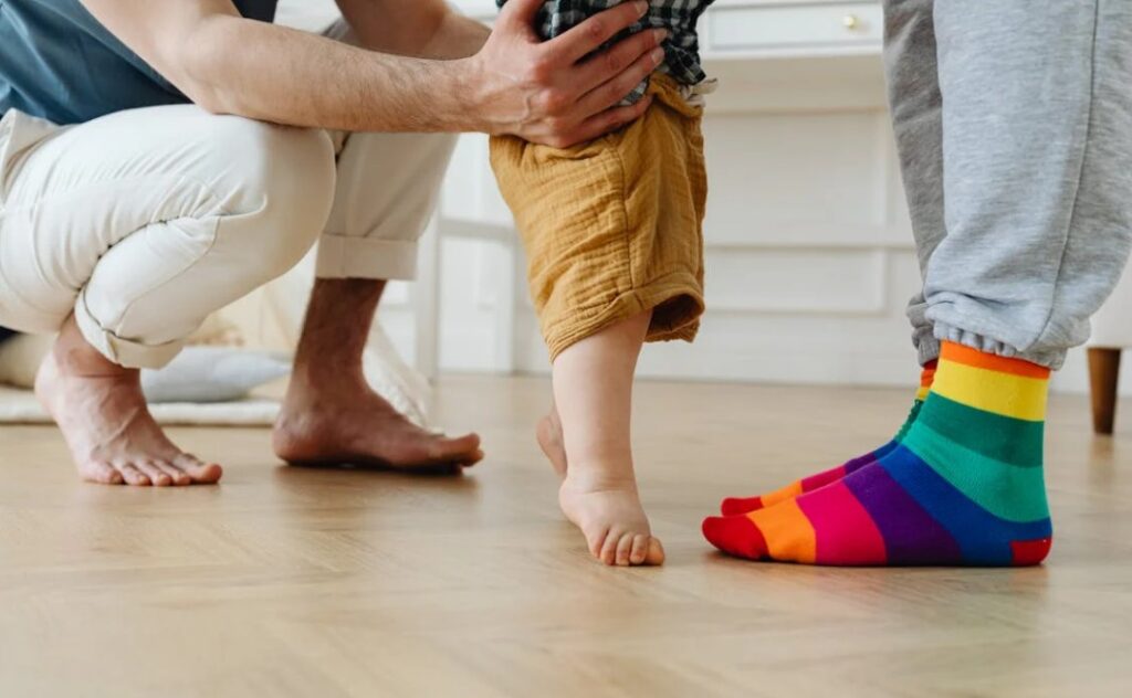 A man supporting a baby learning to take first steps.