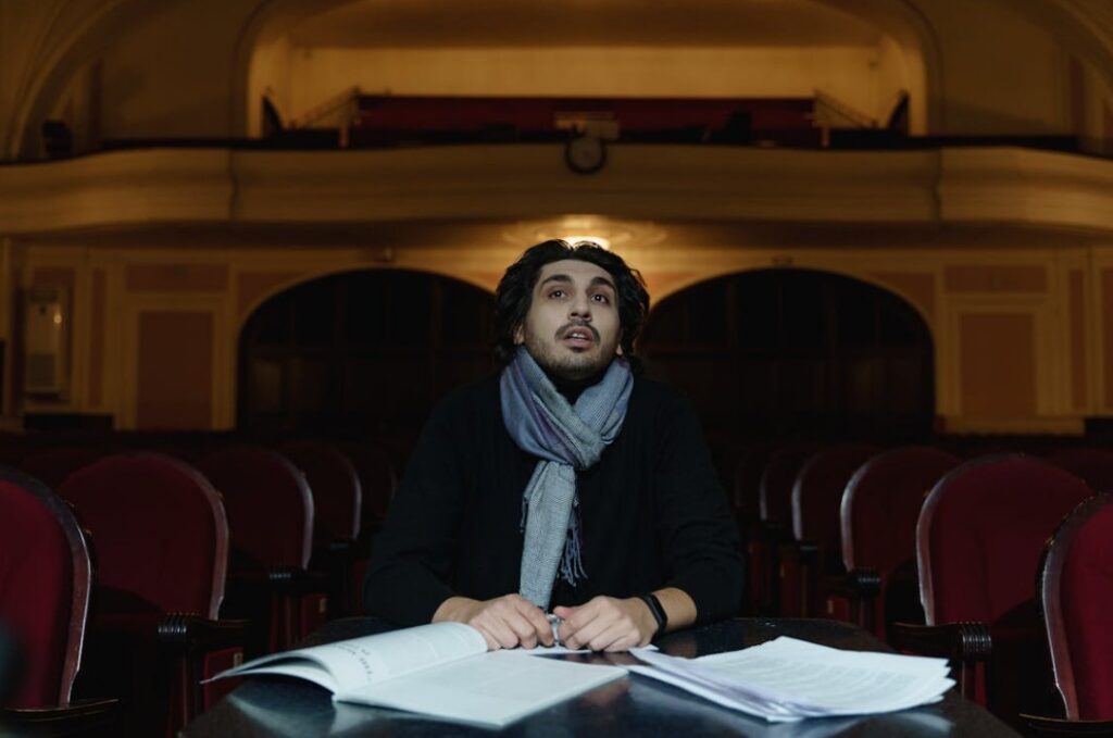 Image of a man in the seating area of a theater with stacks of script paper in front of him.