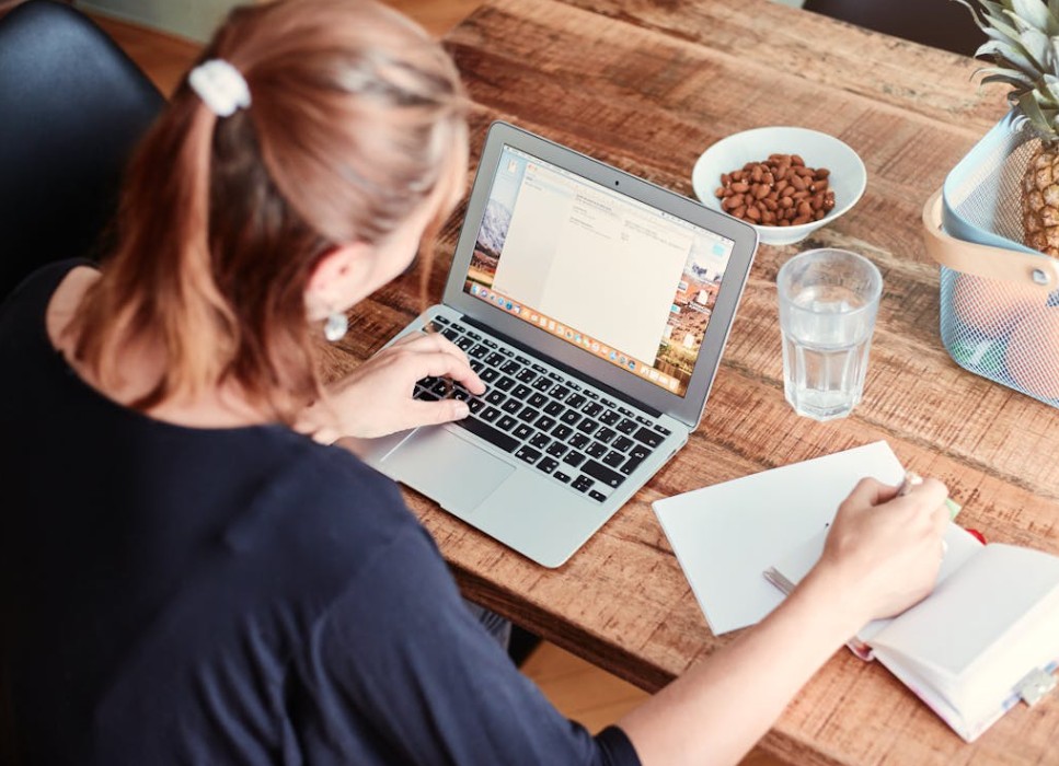 Woman typing and writing in a notebook.