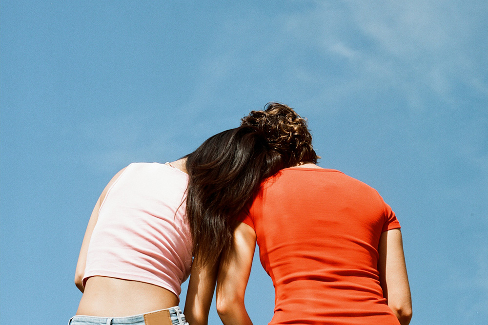 A woman resting her head on another's shoulder to depict characters existing in relationship to one another