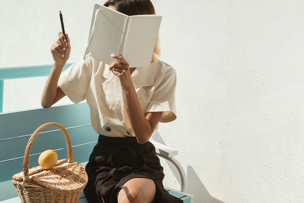 author with a pen in the air with a book over her hand to suggest the incognito nature of a pen name