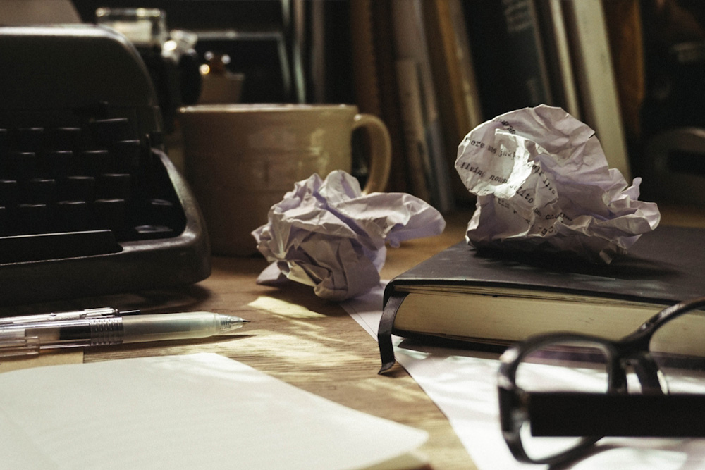A picture of crumpled up pieces of paper next to a typewriter for parity to the author's passage about throwing away hard copies of her work.