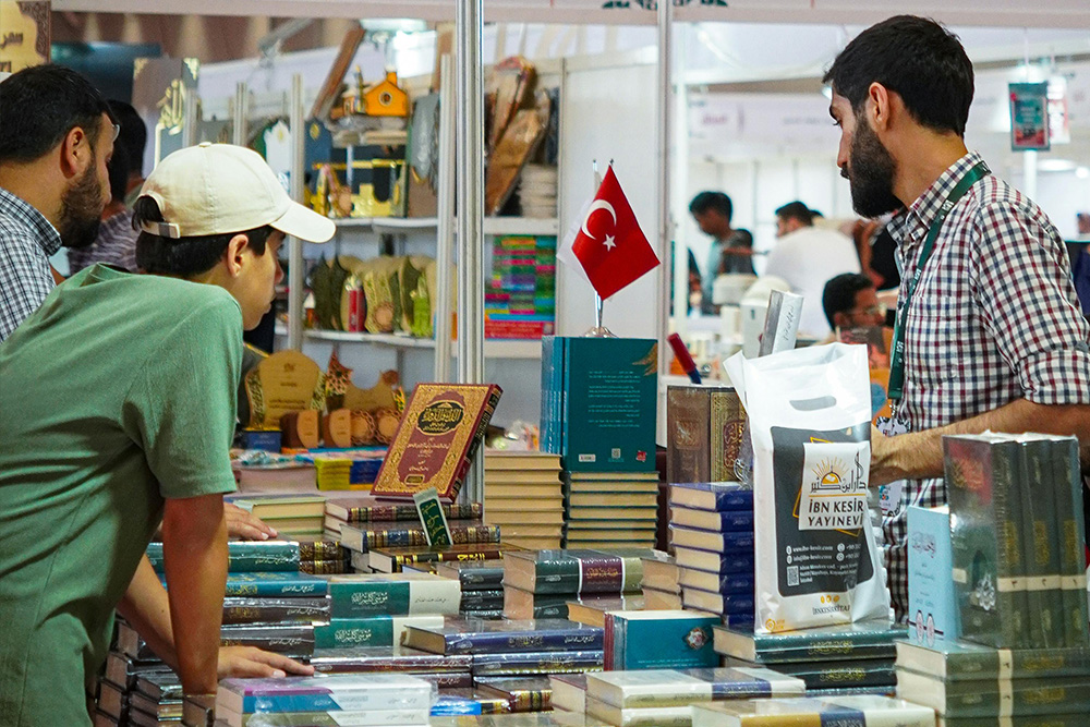 People at a foreign trade show looking over different book cover designs and checking out books to drill a physicality to the necessity of book design. How does your book look in context of a busy marketplace like this?