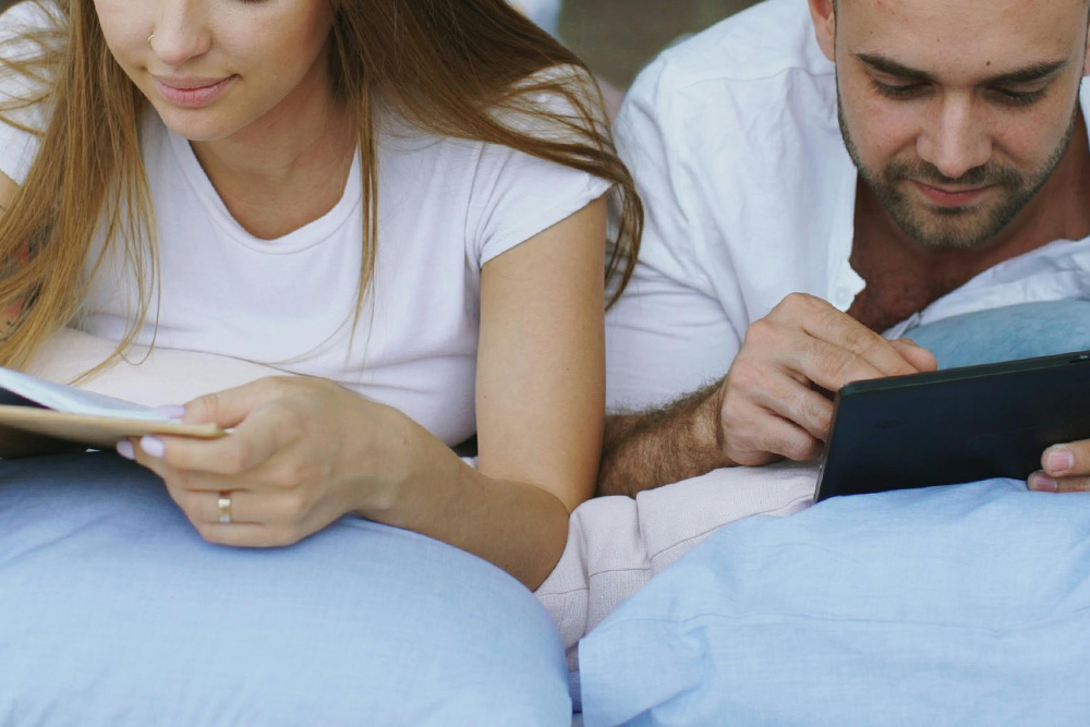 A couple reading peacefully side-by-side on a nondescript book and e-reader respectively