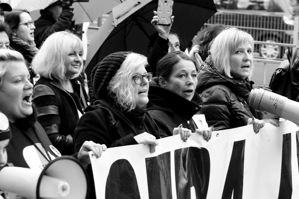 Women protesting in the streets with megaphones to illustrate the daunting nature of using marketing tools to extend the reach of one's books.