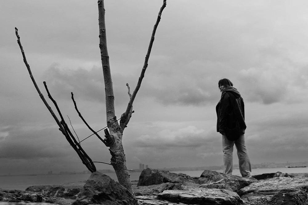 Featured image for Character vs. Society blog, a woman standing alone looking to withered brush that supersedes her hierarchically in the frame to suggest an antagonistic juxtaposition
