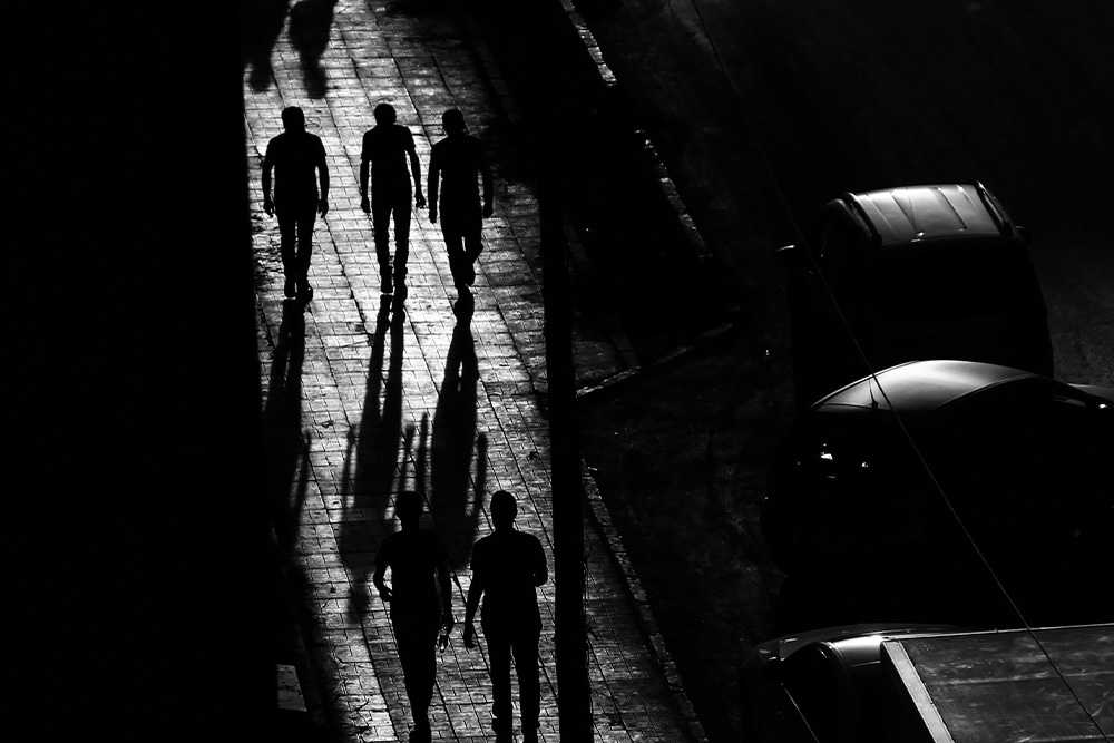 Two shadows color the top of the frame, as five figures walk in tow, suggesting that an audience will follow characters into the darkness (in this case painted by a strong-contrast light to derive the point in a roundabout way)