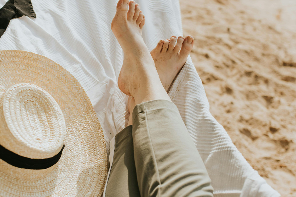 Visualized here, a woman kicking her feet up and putting her hat to rest on a hammock by a seaside view
