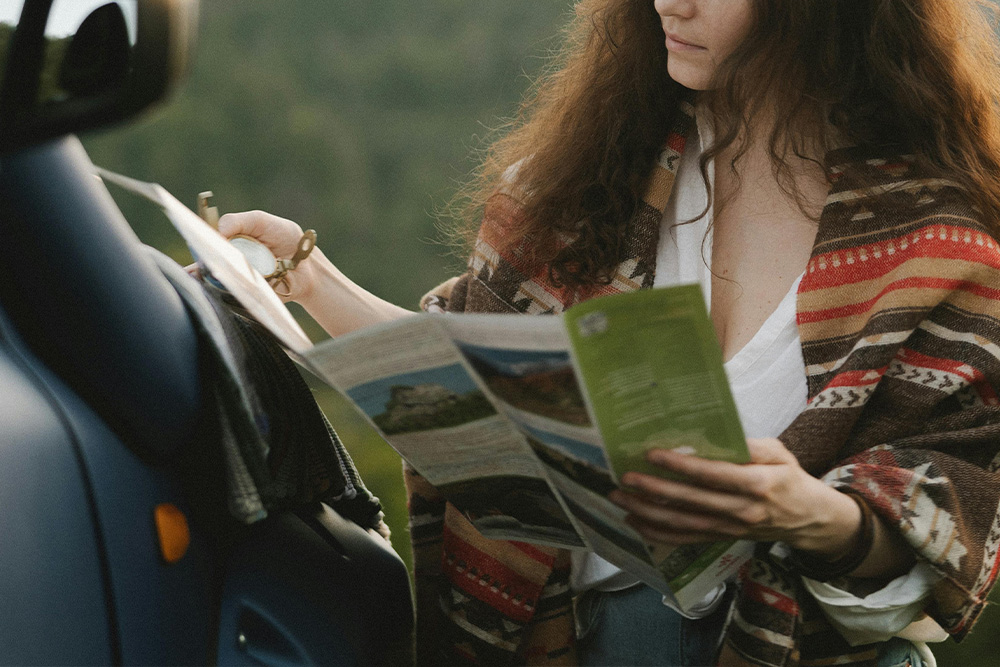 A woman against lush greenery with a map-guide in one hand for the location before her and a compass in the other.