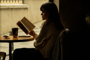 Someone reading a book in the darkness at a café on a very sunny day, emotional themes of relaxedness