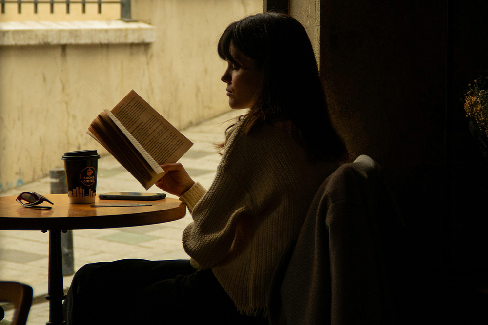 Someone reading a book in the darkness at a café on a very sunny day, emotional themes of relaxedness