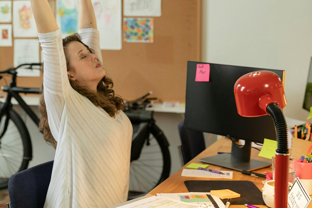 A woman at a desk stretching out with a turned off monitor, suggesting getting ready to get a good day of work in—translating to the process of the writer themself