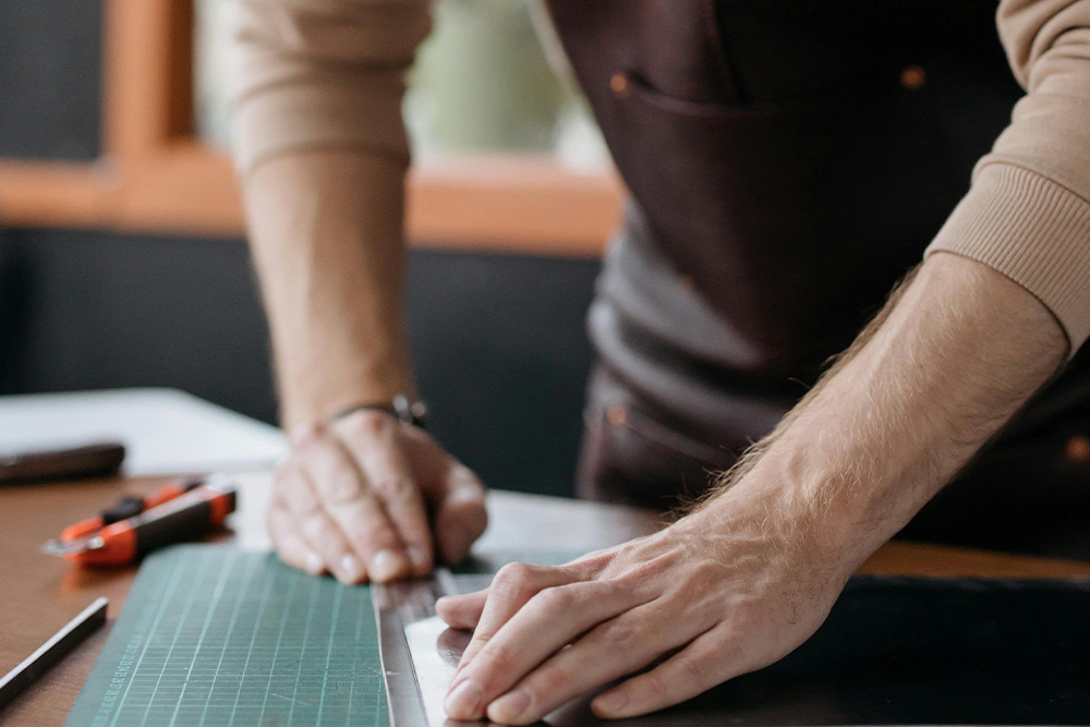 Someone measuring a piece of leather on a marketing board to visualize the question of "book outline: where do I start"