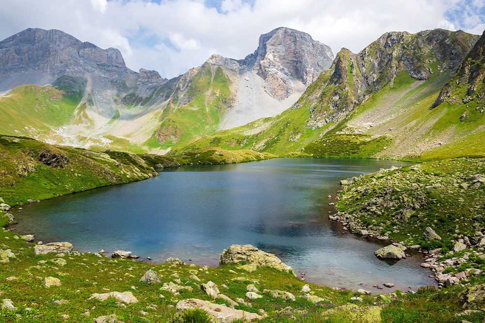 Image of the caucasus mountains used to visualize the 10,000 hour rule and how it can be applied to you, above in the background are high mountain peaks certainly worth climbing but in the foreground is a lake that suggests a serenity and calm in the achievement of joy