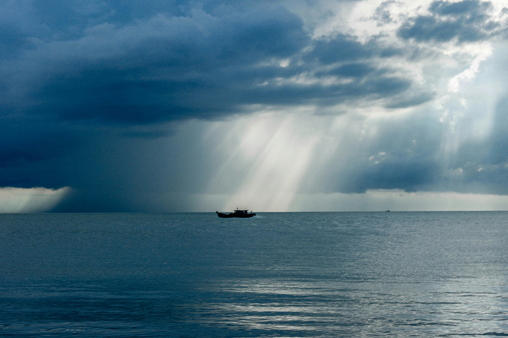 A lone boat silhouetted against a dramatic, stormy sky over a vast sea, capturing nature's power dramatizes character vs. nature conflict