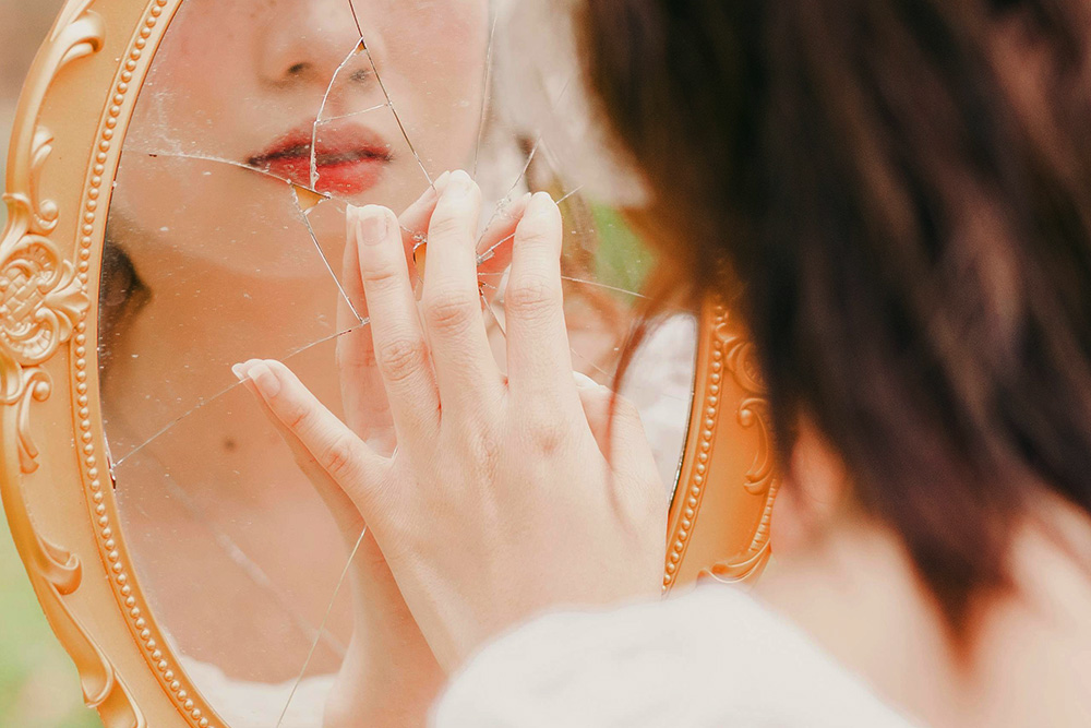 A woman touches a broken reflection, sultry, to suggest the character vs. self conflict in visual form