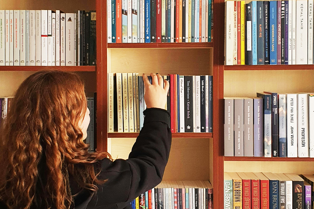 A young person picks a book out from a shelf to suggest the far reach of equipping oneself with the tools on how to self-publish a book