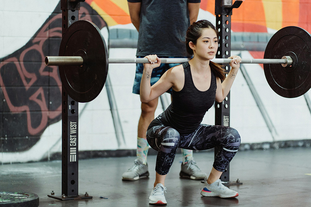 A woman squats weight in understanding how overcoming procrastination might weigh on someone