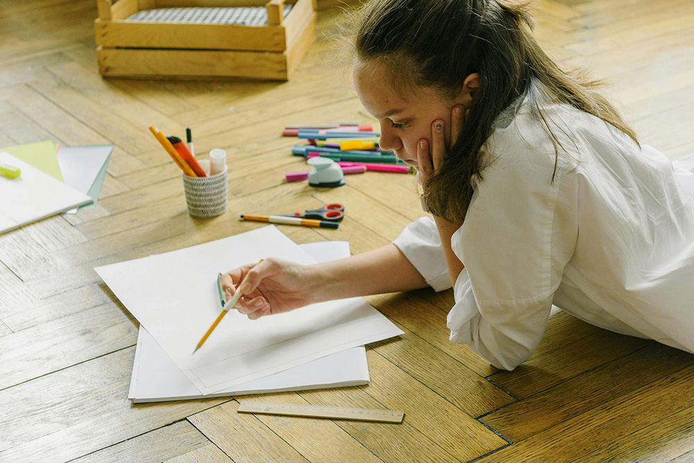 A girl sits with an empty page and all the creative tools that she needs but deep in thought on when to start her writing process, needing blitzkrieg writing to solve her problem