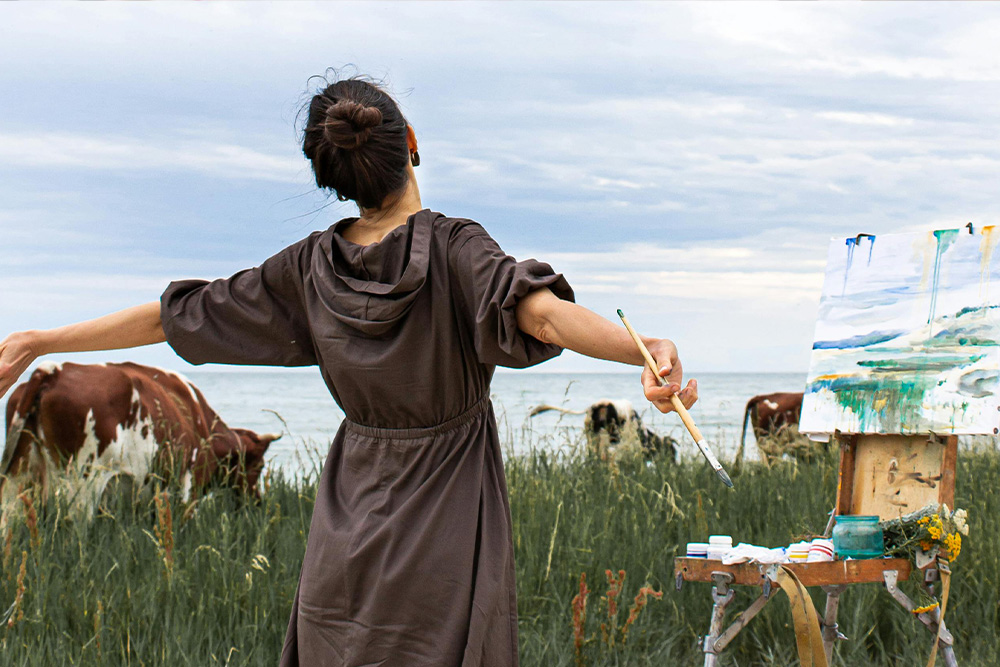 A woman stands, free, atop a cliff working easily on a painting while absorbing the elements as she is freed by the pleasure of blitzkrieg writing