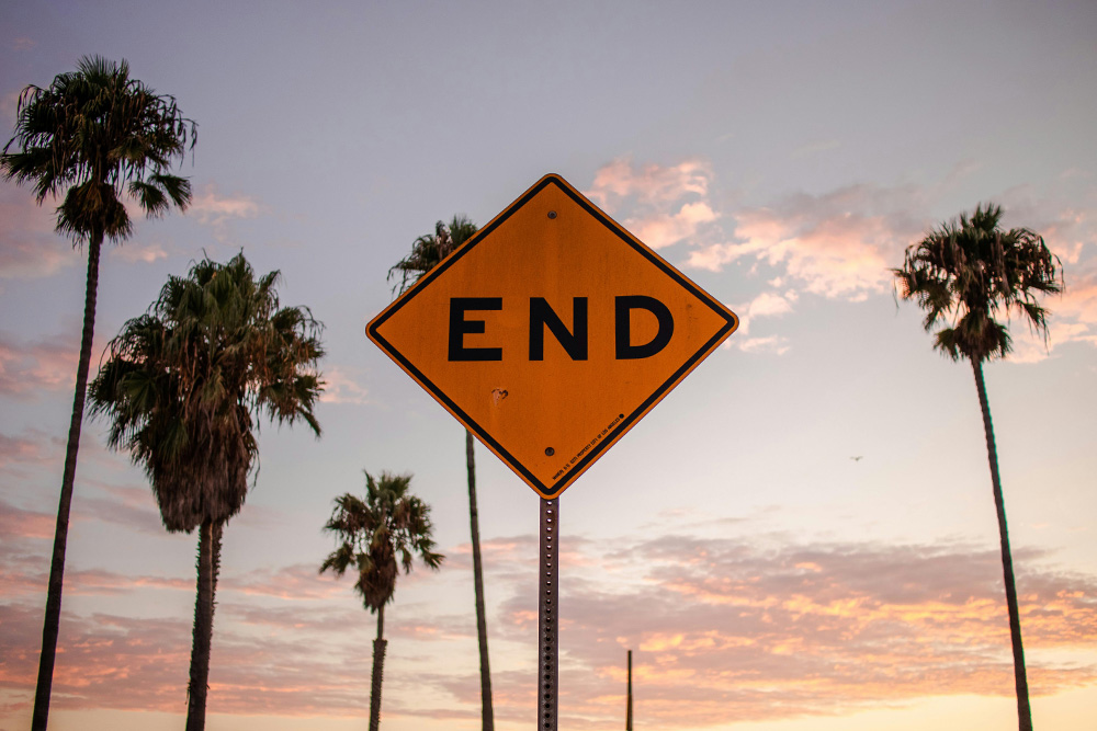 A sign indicates the end of a road at a beach to suggest the joy of concluding the parts of a story