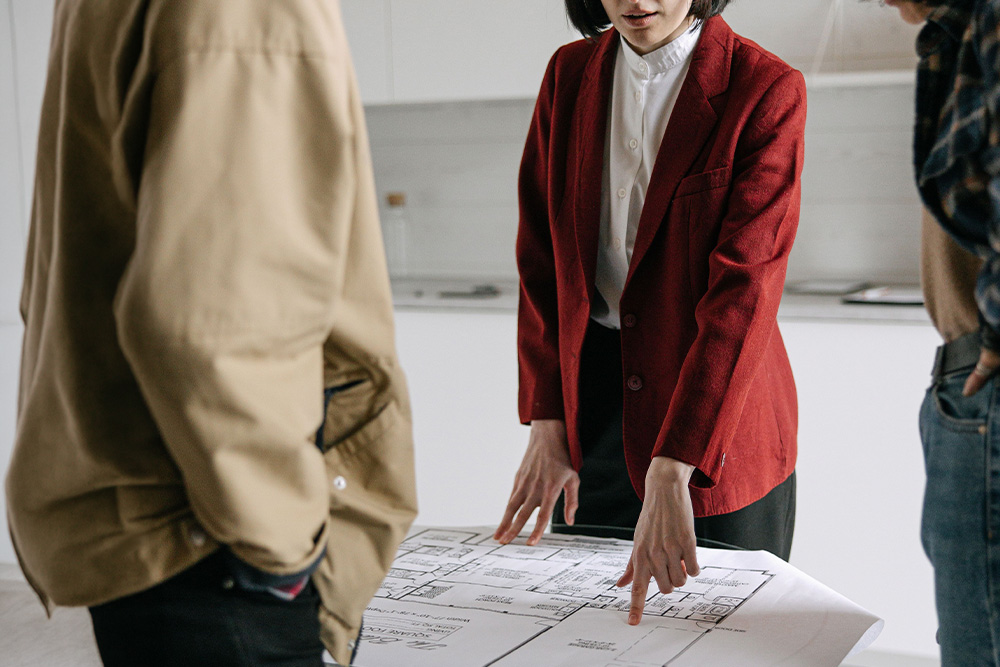 A woman looks at floor plans with two people looking over her shoulder to suggest visual similarity to plot development