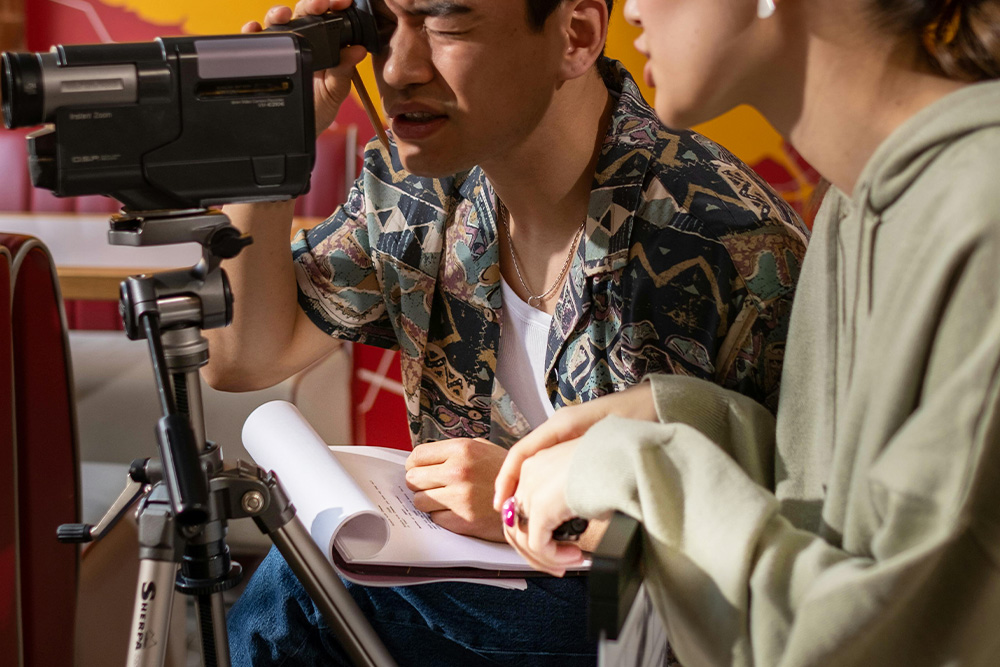 A woman directs a cameraman with a screenplay in hand to suggest that a writer can shine in a different format — What is a screenplay?