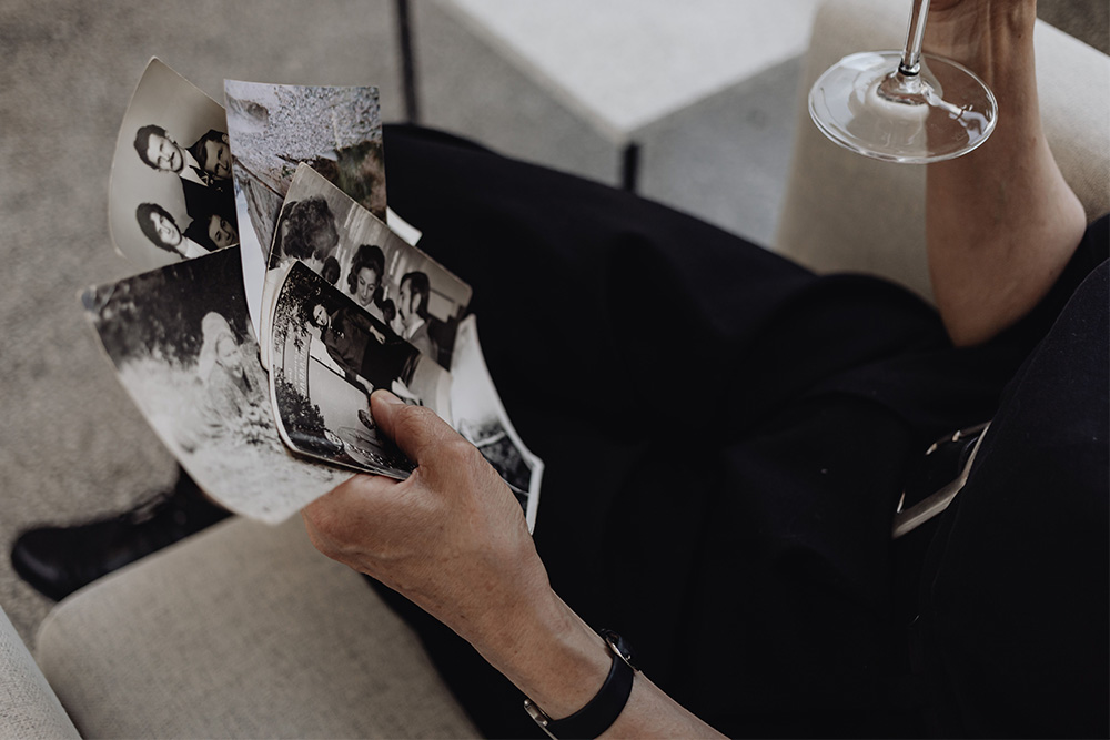A woman sits at a sofa with pictures and a glass of wine, over the shoulder, to suggest advice on writing memoir in not getting too nostalgic or bogged down in details of one's entire life story