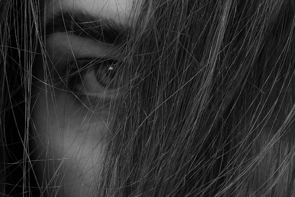 A woman's eye pierces the camera in black and white while being hidden by her hair to suggest that weak memoirs suggest from self-protection