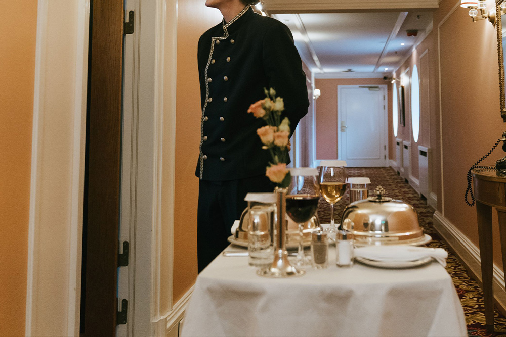 A concierge stands outside of a hotel room to present someone food as a visual metaphor for how to open in how to write a query letter
