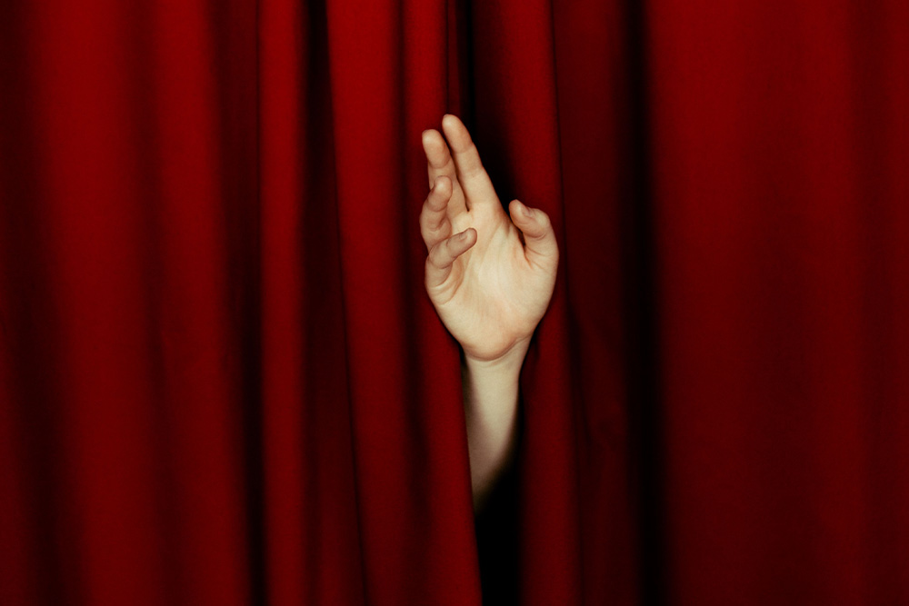 A hand emerges from a curtain to wave goodbye gracefully to suggest how to handle rejection in how to write a query letter
