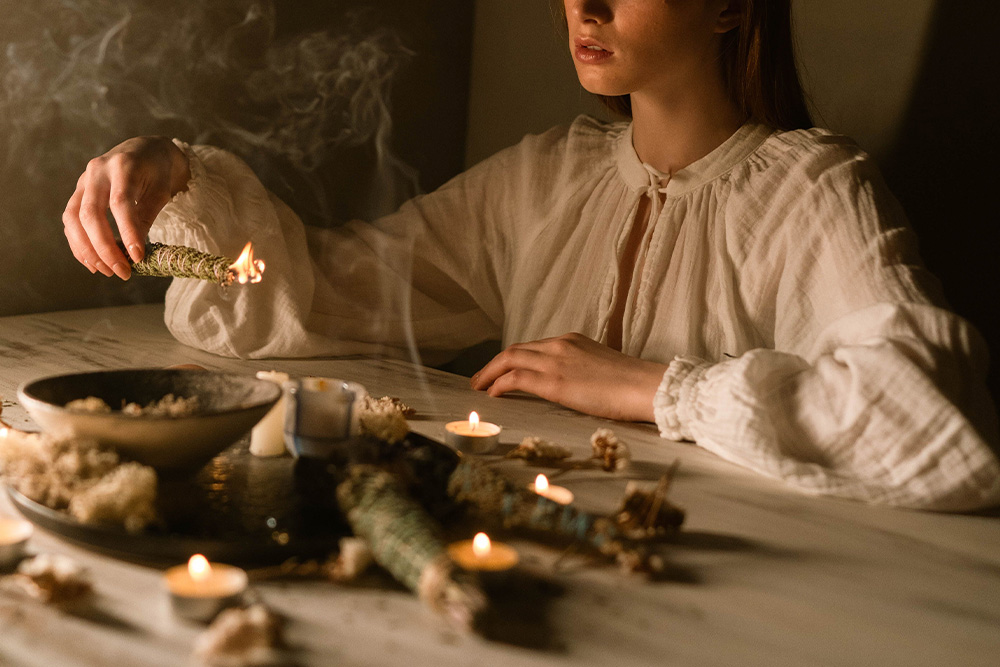 Caucasian woman in white blouse with candles and sage symbolizes where writers go wrong in writing a sage archetype