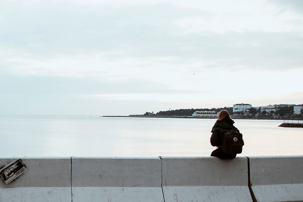 A view of a woman who sits alone by water to create a joy in the third person objective