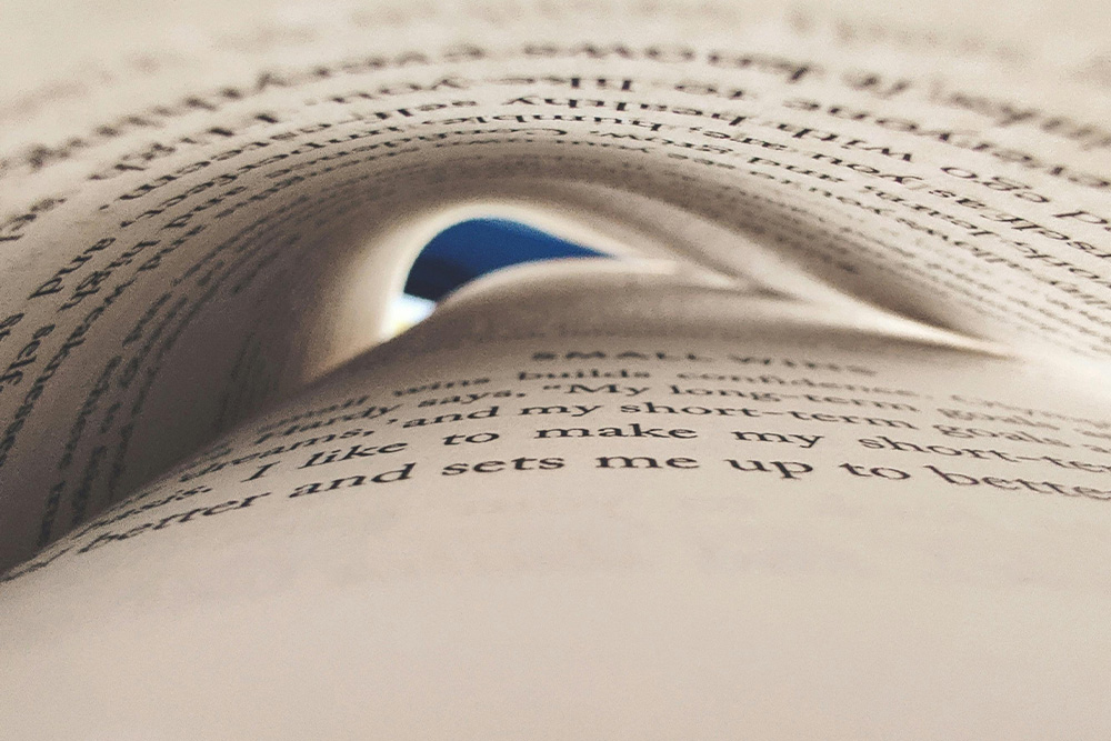An eye-like shape appears in a detail photo of a book with light flittering through the pages to create a sense of trust developed with readers