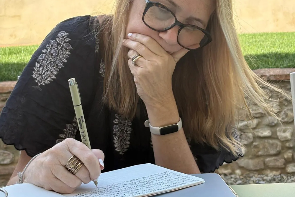A writer is carefully jotting notes over a laptop