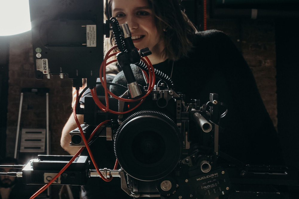 A woman stands in joy behind the camera monitor to suggest that you should be able to enjoy the work of others and imagine a role for another to step into, avoid wearing too many hats as a screenwriter