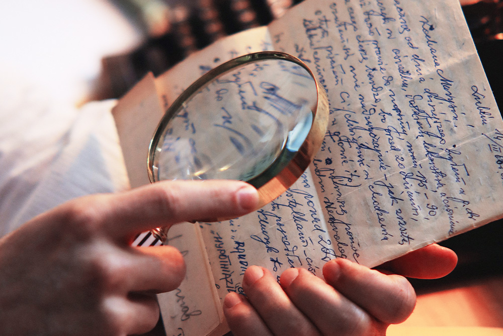 A magnifying glass held up to a piece of writing suggests a close examination of work to observe its subtext