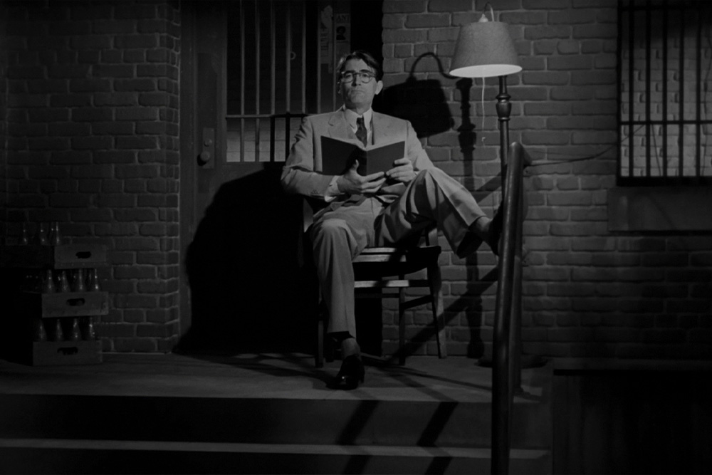 Atticus Finch sits on the porch with an austerity that signals his importance in conveying subtext to the children and audience