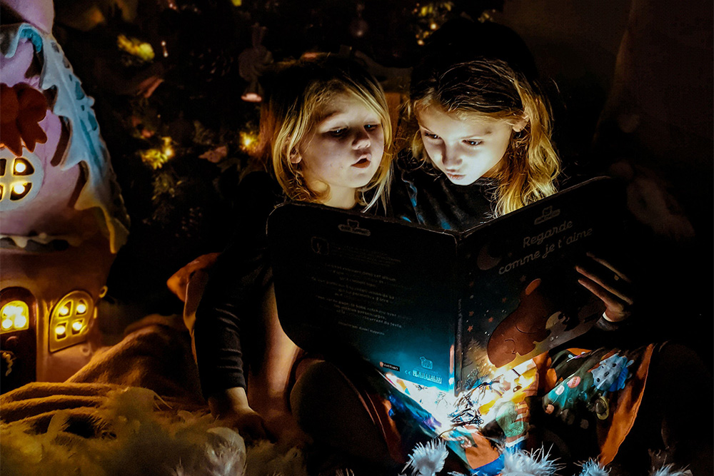 Children sit behind a book and a warm nightlight glows onto their faces to suggest that words have power