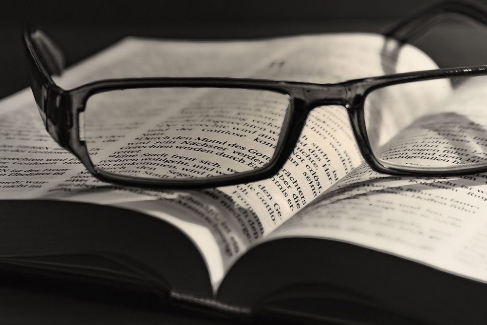 A pair of glasses sit on a dictionary to suggest that words have power and we must take a closer look