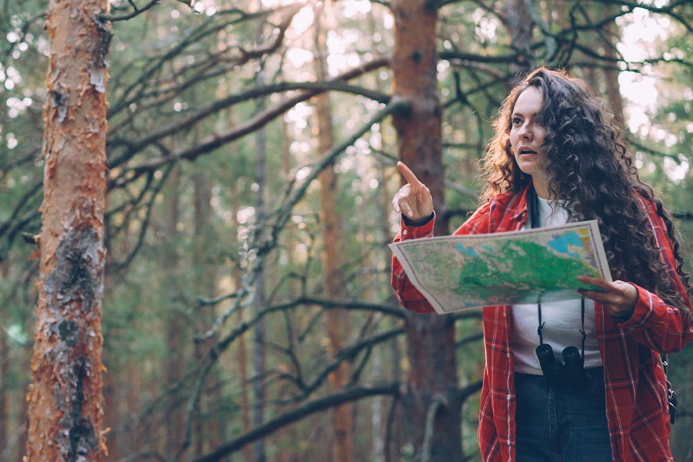 A woman looks out in the foreground with a map in her hand pointing into the distance of lush trees to suggest that avoiding plagiarism has a natural vibe filled with light and leisure