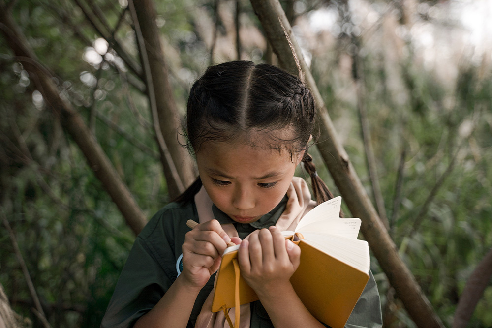 A child with a yellow notebook writes with a concertedness that appreciates a sense of play in the work of writing a cumulative sentence if a writer never has done so before
