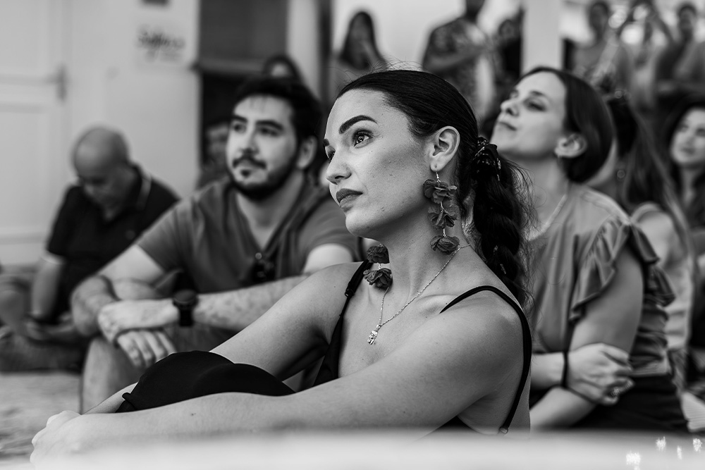 A woman at attention watching someone perform in the foreground and a captive audience behind her suggest the way to write a cumulative sentence that would pull an audience in.