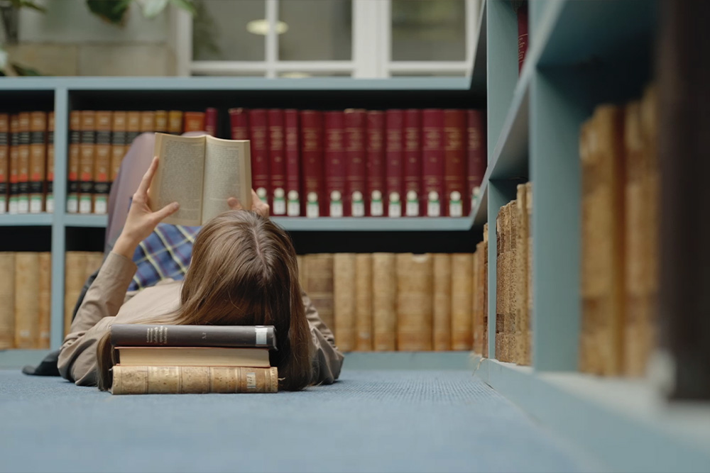 Coolness, relaxed nature of self-editing a novel in a woman stepping away from her book to lie down at the library and enjoy some reading