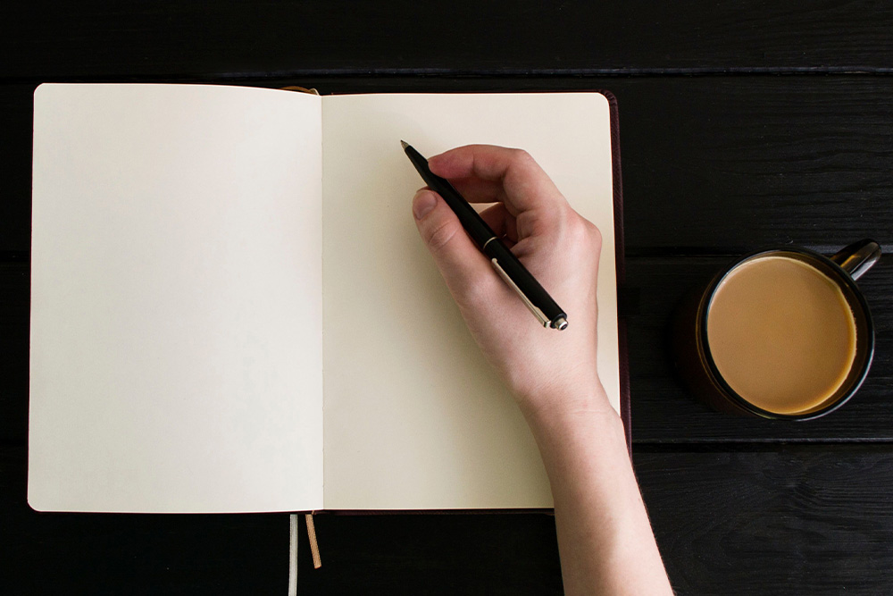 Neat ivory notebook with empty pages and a coffee cup beside it, suggestion of royalty and elegance in how to start a memoir