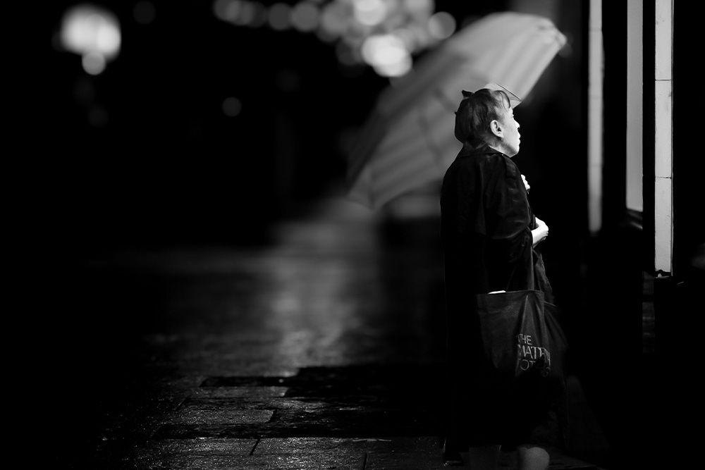 A woman with an umbrella looks sullenly into a window of a storefront to provide internal conflict examples