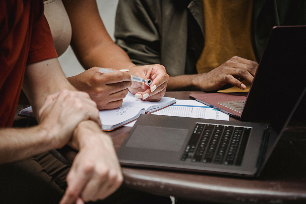 A team of people sat together and reviewing on a notebook and computer suggests the benefits of peer learning, themes of completion