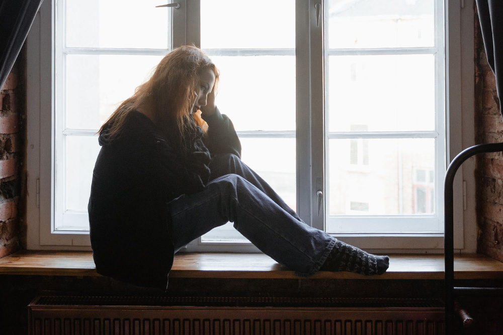 A woman sits sullen on a windowsill to suggest that the scapegoat is the perfect excuse for the main character