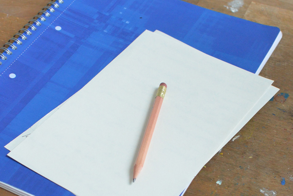An empty page on top of a blue notebook suggests a scholastic focus to writing and not being scared to pick up the pen