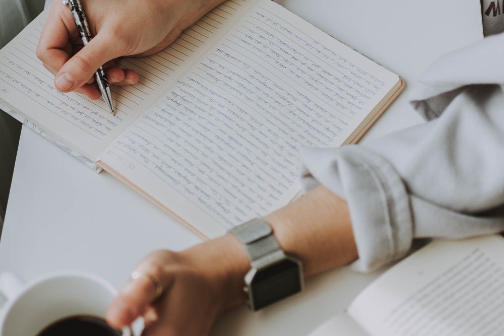 Someone writing journals diligently with a coffee cup to suggest productivity to the audience